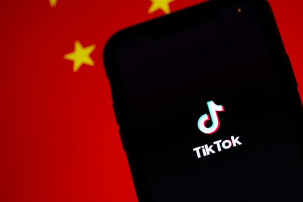 The TikTok splash screen shown on a phone against the backdrop of a Chinese flag