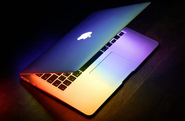 A MacBook shown at a diagonal angle, opening to reveal rainbow lights glowing within