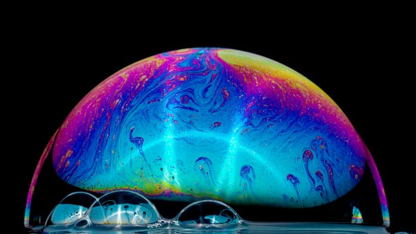 A large soap bubble against a black backdrop featuring smaller bubbles in the foreground
